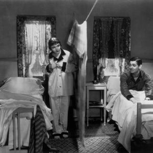 Nainen ja mies valmistautuvat yöpuulle huoneessa, jonka he ovat jakaneet narusta roikkuvalla huovalla kahteen osaan.