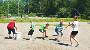 Barn på en sandplan kastar vattenballonger på varandra.