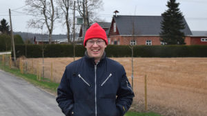 Erik Perklén på hemgården Postis i Lappers i Sjundeå. Erik Perklen med en stubbåker och gården Postis i bakgrunden december 2020.