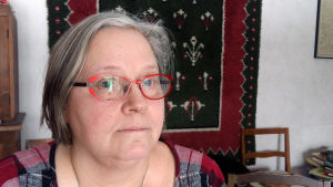 Eva Sjöström blir besviken då hon hör om problemen inom psykiatrin vid ÅUCS. Eva Sjöström, en dam med grånande hår och glasögon med röda skalmar.