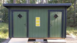 Forststyrelsen har lagt upp varningsskyltar vid vissa besöksmål. Vid toaletterna varnas besökaren om att man inte kan garantera att toaletterna är hygieniska på grund av coronaviruset. En grön liten byggnad med offentliga toaletter. På fasaden finns gula varningslappar.