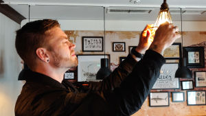 Aaro Tukiainen-Lindroos berättar att man förnyat inredningen i baren just innan viruset slog till. En ung man skruvar på en hängande lampa.