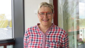 Pirkko Grönroos från Tandläkarförbundet förutspår att den offentliga tandvården får problem efter pandemin. En kvinna med blont kort hår och glasögon och röd-blå-vitrutig skjorta står ute på en inglasad balkong. Hon ler stort.