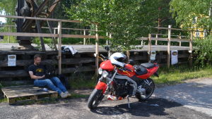 Niklas Montonen pendlar till Helsingfors, för det mesta åker han med motorcykel. niklas jobbar på sin dator i skuggan, bredvid finns hans röda motorcykel.