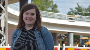 Här är Emilia Nyberg, konstnären bakom Kariskartan. En kvinna står på Karis järnvägsstation. Det är en byggarbetsplats med gul-röda skyddsstaket bakom henne.