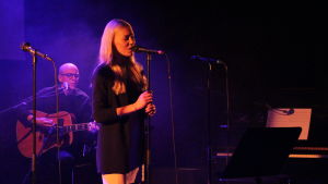 Annette Lundell sjunger bland annat She will be loved av Maroon 5. En blond kvinna sjunger på en scen. En man spelar akustisk gitarr.