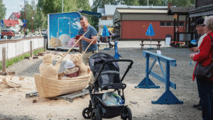 En liten passagerare i Timo Nevalainens verk Kalassa. Mies ottaa kuvaa pienestä lapsesta, joka on veneen mallisessa puuveistoksessa