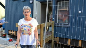 Asta Lehtola tyckte att husen var fina. En kvinna står framför dörren till ett blått trähus.