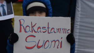 Också små barn deltar i demonstrationen. Ett asylsökande barn visar upp en skylt med texten "Rakastamme Suomi".