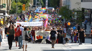 Pridemarschen ringlade genom Åbo centrum. Pridemarsch med många personer vandrar genom Åbo centrum.