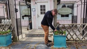 Gustav Söderström har satt ut vårblommorna. En man står utanför ett ljusrött trähus och petar med blommor i en kruka.