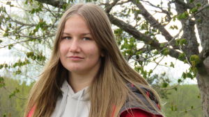 Det råkade sig också så att Emilia Kytöpuro var på en utlandsresa just när distansundervisningen tog vid, så för hennes del har det känts som en extra lång tid att vara borta från skolan. En 15-årig flicka med långt ljusbrunt hår. Hon har en röd, vintät jacka på sig och en grå munkjacka under. Hon ser in i kameran, ser allvarlig ut. I bakgrunden ett träd (lönn) som håller på att få löv. Lövsprickning.