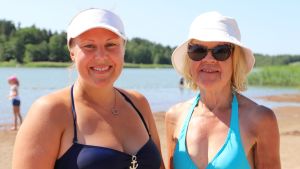 Linda Silván och Kaisa Viitala. En yngre och äldre kvinna som båda har ljust hår och vit hatt och baddräkt står på en simstrand.