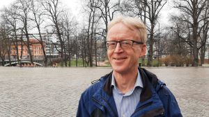 Henrik Saxén, professor i värmeteknik vid Åbo Akademi. Henrik Saxén, en man med ljusr hår, glasögon och blå rock står en kylig vårdag vid ett torg med nubbstenar. I bakgrunden syns kala träd och en bro.