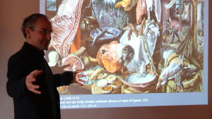 Fred Andersson, universitetslärare vid Åbo Akademi. Fred Andersson står framför en målning av sharkprodukter.