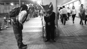 Nuori nainen ja kissapäinen mies tervehtivät toisiaan japanilaisella asemalla. Kuva elokuvasta Terveisiä Fukushimasta.