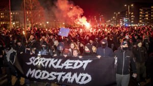 I Danmark frågar man sig om Men in black Denmark kommer att bli en mer bestående rörelse. Bilden är från en demonstration i januari. Ett folkhav av människor mitt i en stad. I förgrunden syns några personer med en stor svart banderoll med vit text på. Många har munskydd och de flesta är klädda i svarta kläder. Folkhavet lyses upp i rött av en bengalisk eld.