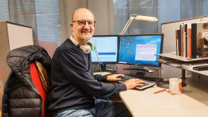 Marko Wahlström gillar att jobba med lokaljournalistik. En man sitter bakom ett skrivbord. Han tittar in i kameran och ler.