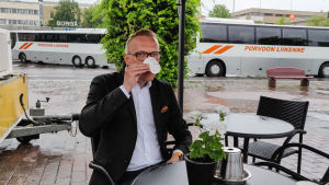 En sak som är bra med att jobba hemifrån är att det är nära till kaffekokaren, konstaterar Ujula. Torgkaffe är det heller inget fel på. En man i kavaj sitter utomhus vid ett café och dricker kaffe ur en pappmugg.