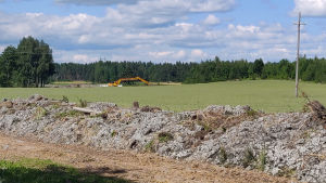 Jordmassorna ska bredas ut på åkern. Stora jordvallar på en åker. Långt borta syns en gul grävmaskin.