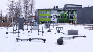 Utegymmet vid Nickby Hjärta. Förutom olika sorters ställningar finns också en gunga. Det finns också instruktioner för hur ställningarna kan användas. Olika ställningar och gymredskap i snön utanför en grön byggnad.