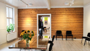Här ska Galleri Theodor flytta in. En man står i en dörröppning till ett ljust rum med en stockvägg. På ett bord finns en vas med solrosor.