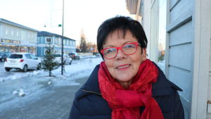 Hilkka Wilhelms. En kvinna med mörkt hår och röda glasögon. Runt halsen har hon en stor röd halsduk.