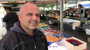 Twana Hana är torgförsäljare i Sjöbo och bor själv i Malmö. Han har aldrig stött på rasism eller tråkiga kommentarer i Sjöbo. Torghandlaren Twana Hana med lådor av bär och frukter i bakgrunden.