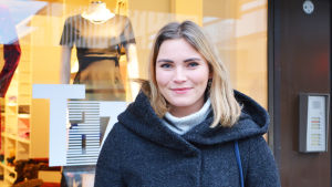 Olivia Andersson. En ung kvinna står utomhus framför ett butiksfönster. Hon ler och tittar in i kameran.