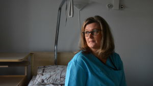 Sjukskötare Nina Öhman är jätteglad över att verksamheten kom tillbaka till Karinahemmet. Kvinna sitter på en sjukhussäng och tittar snett över axeln ut genom fönstret.