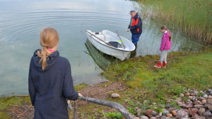 Barnen är besvikna på algläget vid stranden - men det är bättre nu än det kunde ha varit utan Daphnias engagemang. Två barn ser på när en äldre man puttar ut en plastbåt i sjön Dragsfjärden.