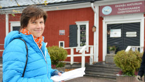 Jonna Engström-Öst talar varmt om Ekenäs Naturum. Själv besöker hon stället ett par, tre gånger per år. Jonna Engström-Öst står med en bunt papper i handen. I bakgrunden skymtar en röd byggnad.
