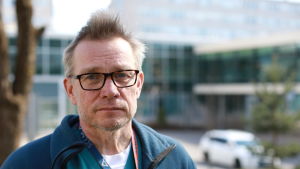 Överläkare Tero Varpula säger att då väggen inom intensivvården kommer emot så handlar det om brist på personal, inte brist på medicinsk utrustning. En man i blå jacka, glasögon och kort hår tittar allvarligt in i kameran. Han står utomhus och bakom honom skymtar suddigt en stor vit byggnad med en glasfasad, parkerade bilar och gräsmattor i spirande grönska.