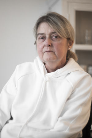 Tuija Wahalahti bodde tidigare i Kyrkslätt. Där hade hon inte lika stora problem med att få tag på assistenter. En äldre kvinna ser rakt in i kameran. Hon ser allvarlig ut. Bakgrunden är vit, och där syns en bokhylla.