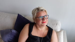 Mela Nyholm i sitt vardagsrum. Mela, Mikaela Nyholm i sitt hem i soffan, där hon ser ut på björkarna. Maj 2019
