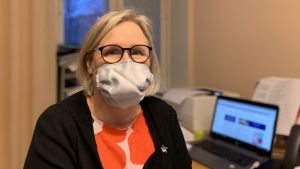 Tiina Böling, ledande socialarbetare vid barnskyddet i Vasa stad, befarar att de ekonomiska svårigheterna som pandemin orsakar börjar synas på allvar först längre framöver. Kvinna i kontorsmiljö, bär munskydd.