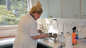 Dricksvatten filtreras av Kristiina Salmiharju. Via filtrering kan man upptäcka bakterier. En kvinna i vit labbrock står och jobbar i ett laboratorium.