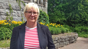 Pia Rosengård-Andersson Pia Rosengård-Andersson med husfasad och natur i bakgrunden.