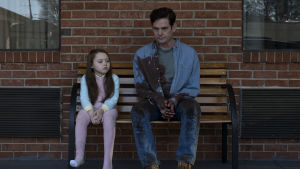 Nell (Violet McGraw) och Hugh Crain (som spelas av Henry Thomas även känd som Elliot i filmen E.T.) Nell (Violet Mcgraw) och Hugh Crain (Henry Thomas) sitter bredvid varandra på en bänk.