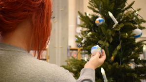 Leila Karlsson har fått ta emot julklappshjälpen redan under flera år. En kvinna med rött hår håller i en julgranskula som hänger i en julgran.