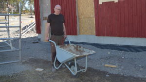 Bromarvs bästa arbetshäst, Henrik Huldin, gnor på med både anställda byggare och frivilligjobbare för att allt i hamnen ska bli färdigt till säsongsöppning senare i vår. En man med skottkärra vid ett bygge. Bakom ett halvfärdig byggnad med väggar målade i rödmylla.