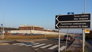 Skylt som visar att man ska svänga in till Åbo fängelse och Psykiatriska sjukhuset för fångar. Fängelset i Starrbacka är en byggnad i rödtegel, omgiven av en vit mur och taggtrådsstängsel.