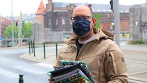Mehdi har som många andra Brysselbor kommit för att köpa tyg för munskydd. Brysselbon Mehdi har kommit för att köpa tyg för att kunna tillverka munskydd till sig och sin familj. Mehdi står med en hög tyger i sin hand på gatan utanför textilaffären gröna hunden. Han har ett svart munskydd.