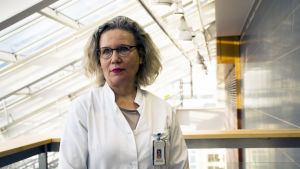 Maritta Kilpeläinen, överläkare vid lungkliniken i Åbo. Maritta står i vit läkarrock under ljusa takfönster och tittar ut ur bild.