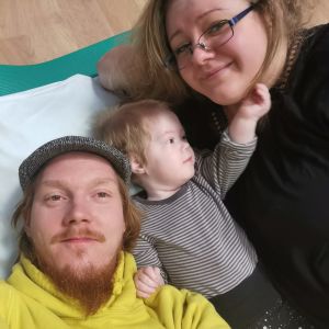 Familjen väntar på att kunna bo tillsammans hemma i Forsby. Två föräldrar och ett barn ligger på en säng.