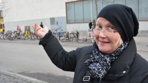 Virpi Tervonen. Virpi Tervonen, en dam med glasögon och svart mössa, pekar mot Åbo huvudbibliotek.