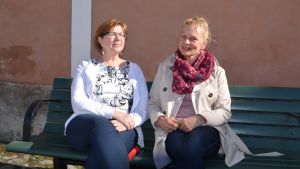 Ordförande Pilvi Saarenpää och sekreterare Eija Oksanen arbetar för att de första stugorna ska kunna byggas i Humleberg nästa år. Arkivbild. Eija och Pilvi på en bänk i solskenet.