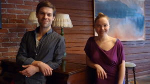 Jon och Victoria i den gamla skolsalen. Här ordnas också musikkvällar. Jon Lindström och Victoria Lindqvist lutar sig mot en flygel i en sal inne i den gamla skolan i Tenala, numera Villa Christine.
