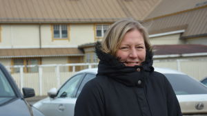 Sari Fredriksson. Sari står utomhus i en svart jacka. I bakgrunden FBK-huset i Pargas.