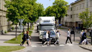 I trafiken bär alla ett ansvar för tryggheten. Fotgängare korsar vägen vid ett övergångsställe. Bilar väntar på sin tur.